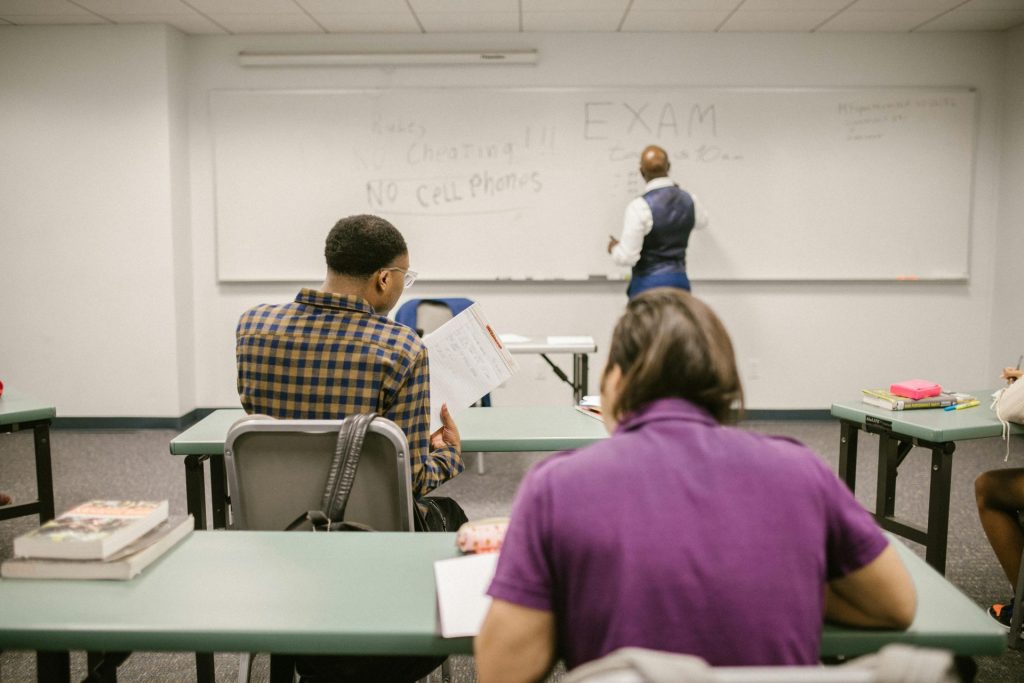 Students in a college classroom taking an exam with rules written on the board.