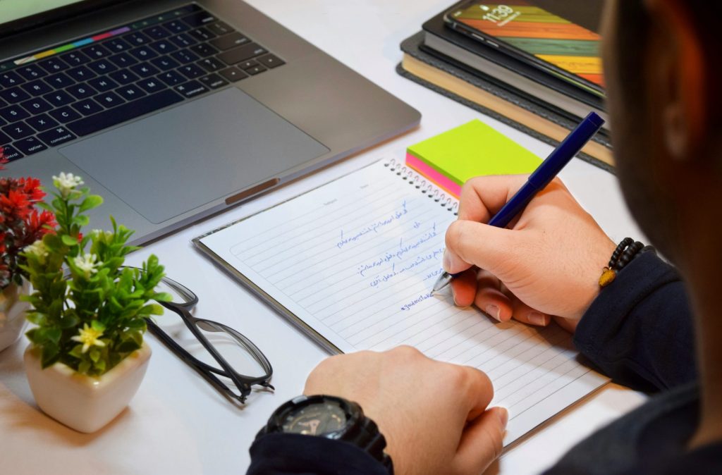 person holding blue pen writing on white paper
